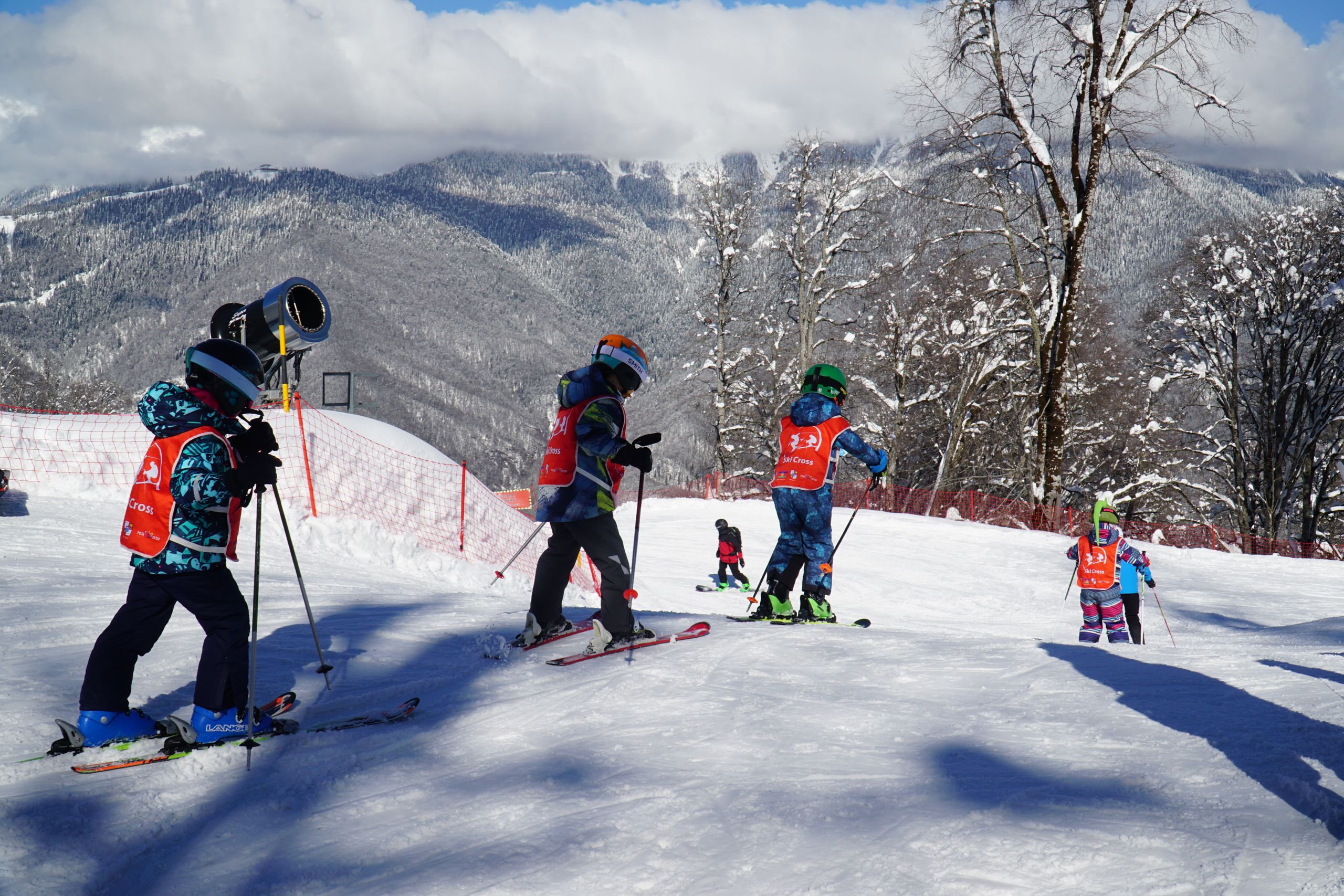 Group of children learning to ski on a snowy slope in Adlerskiy, Russia, under clear winter skies.